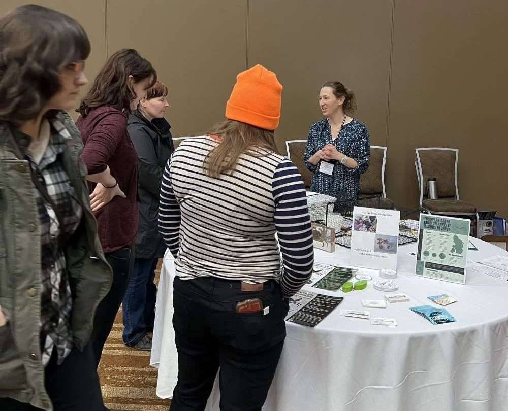 Staff share invasive species outreach material at display booth with visitors