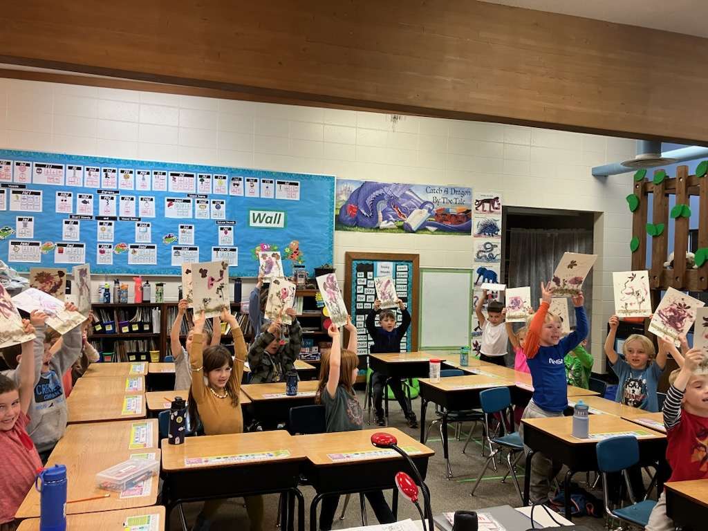 Elementary school students proudly hold up their artwork created using plants found in the peatland