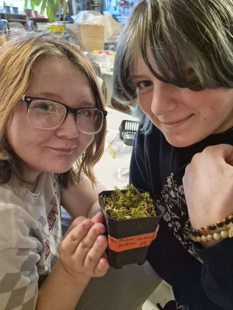 two students look at moss and peat in a small cup.