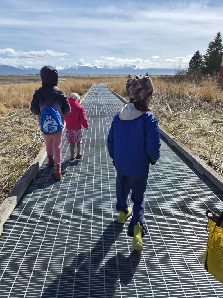 Young kids walk on a board walk over a salt marsh