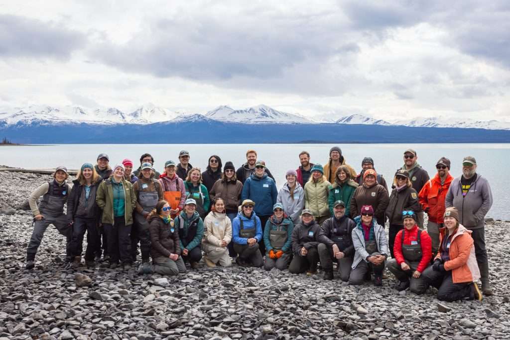 large group photo of people facing camera on beach with mountain range behind them